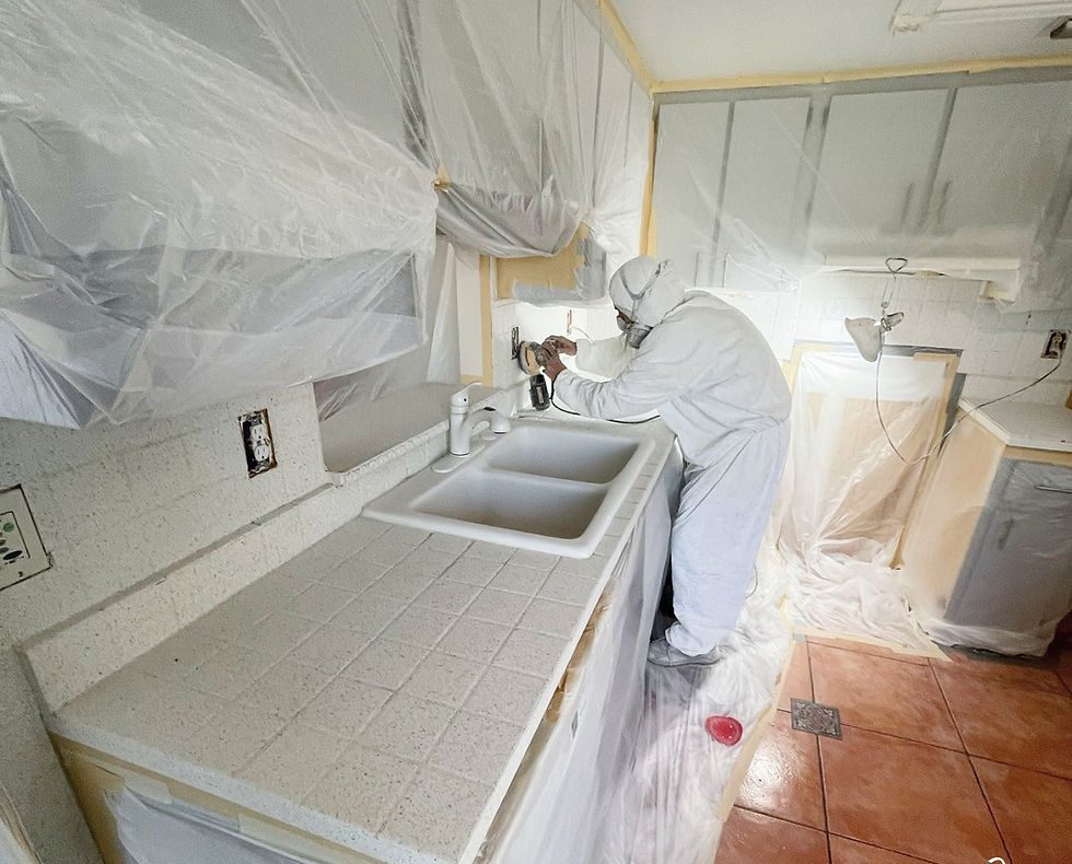 Technician in protective gear spray-applying a resurfacing coating, work area fully masked