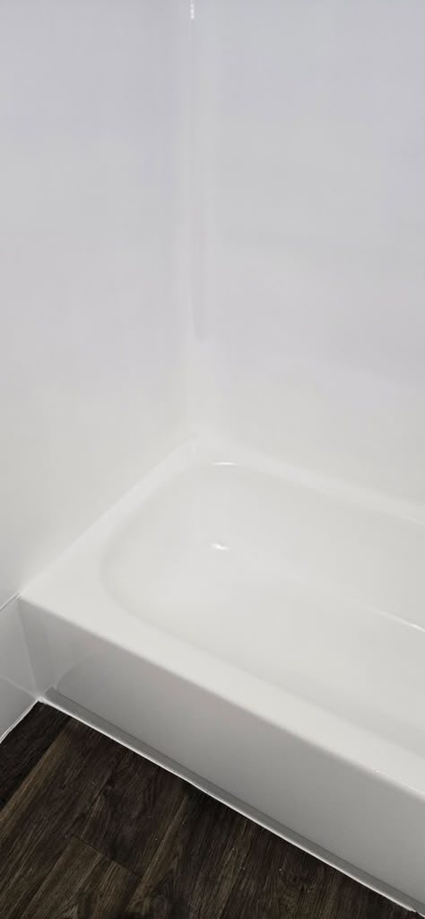 The same bathtub after resurfacing, glossy white with dark wood-look flooring